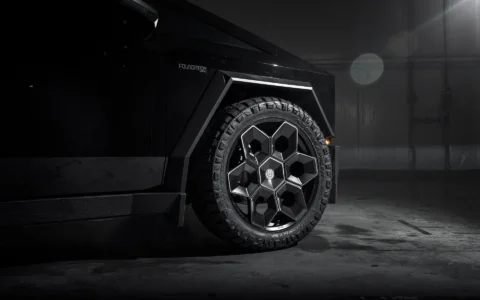 Side view of Tesla Cybertruck equipped with Unplugged Performance 24-inch Cybrhex Wheels in Satin Black, captured in a high-contrast lighting setup to emphasize the truck's angular body and robust wheels.